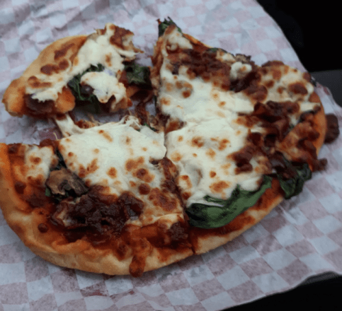 A slice of pizza topped with cheese, spinach, and meat, resting on a checkered paper.