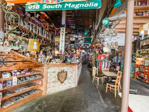 A vintage shop interior featuring antiques, records, clothing, and eclectic decor, with a wooden counter and shelves.