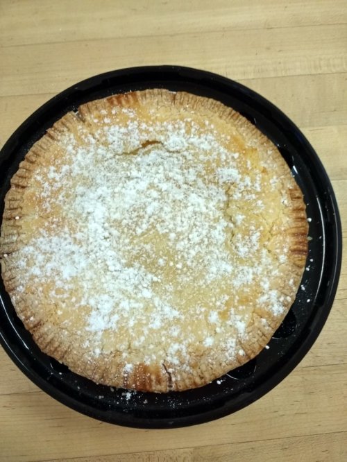 A round pie with a golden crust, dusted with powdered sugar, placed on a black tray.