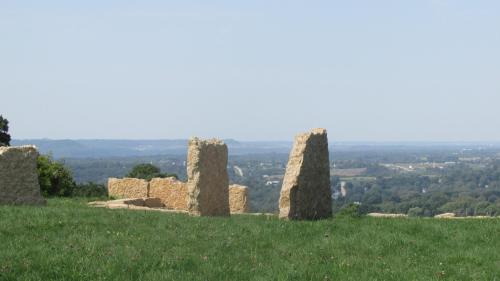 Stone structures on a grassy hilltop with a panoramic view of the landscape and distant hills under a clear sky.