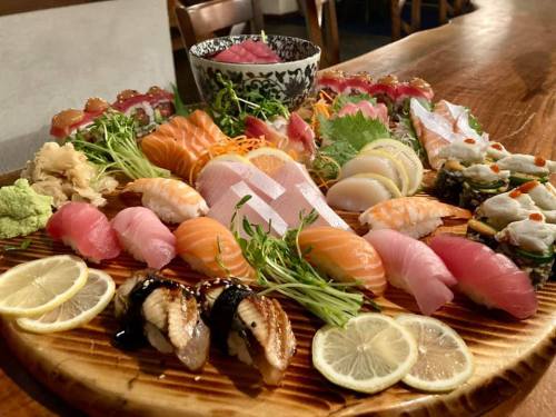 A beautifully arranged platter of various sushi, sashimi, and garnishes, with lemon slices and a decorative bowl in the background.