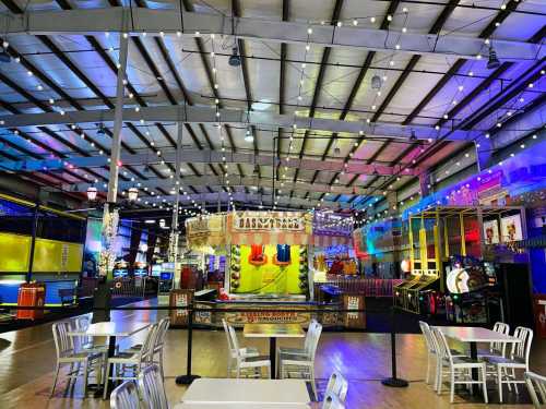 Brightly lit indoor amusement area with games, rides, and tables, featuring colorful decorations and string lights.