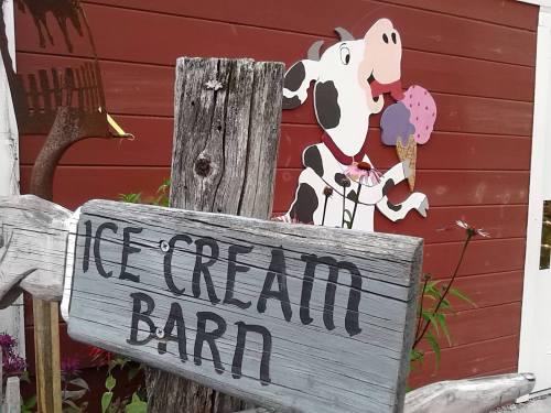 A wooden sign reads "Ice Cream Barn" with a cartoon cow holding an ice cream cone in front of a red barn.