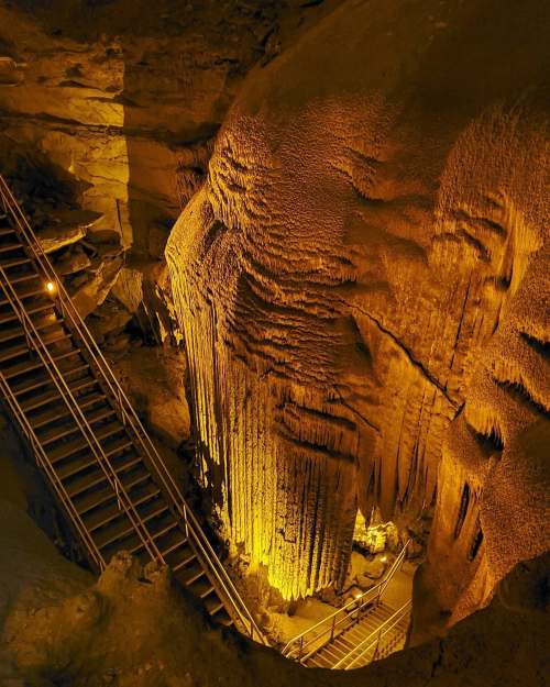 A dimly lit cave with intricate rock formations and a staircase leading down into the cavern.