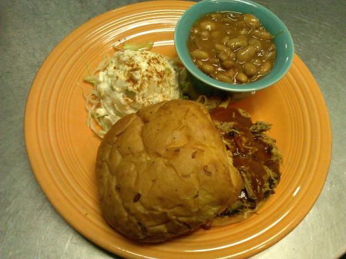A colorful plate featuring a pulled pork sandwich, coleslaw, and baked beans in a blue bowl.