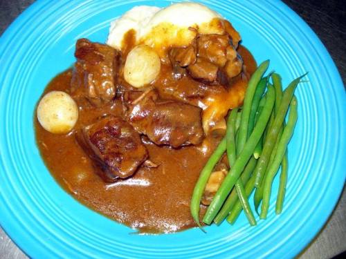A blue plate with beef stew, mashed potatoes, pearl onions, and green beans.