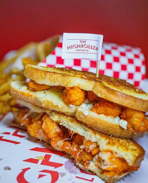 A close-up of a grilled sandwich filled with shrimp and cheese, topped with a small flag, alongside crispy fries.