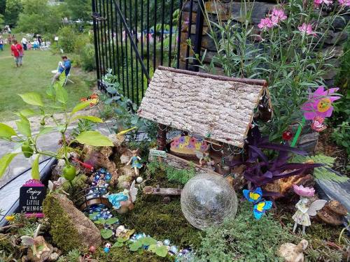 A whimsical fairy garden with a small house, colorful flowers, butterflies, and decorative stones.