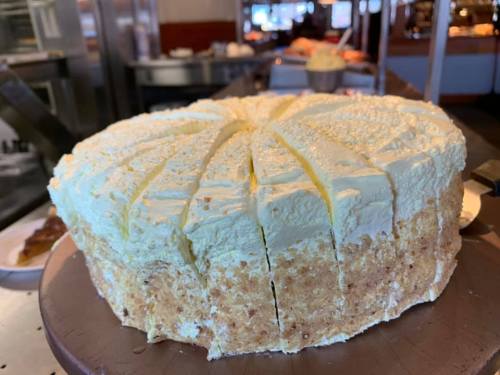 A round cake with a light yellow sponge and creamy white frosting, sliced into even pieces, displayed on a serving tray.
