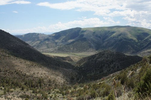 A panoramic view of rolling green mountains and valleys under a partly cloudy sky.