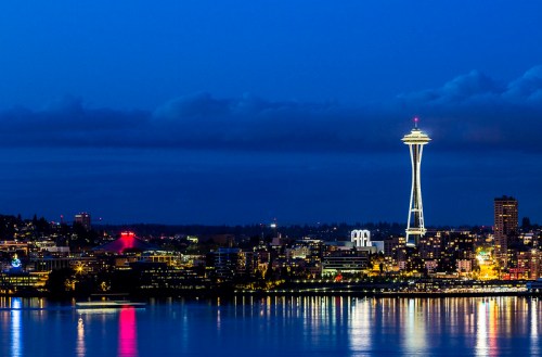Seattle skyline at dusk, featuring the illuminated Space Needle and reflections on the water.