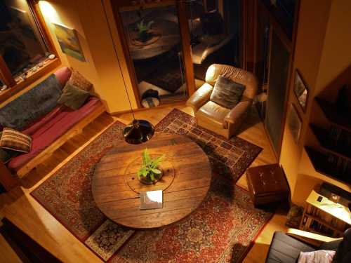 Cozy living room with a round wooden table, plush seating, and warm lighting, featuring a plant centerpiece.