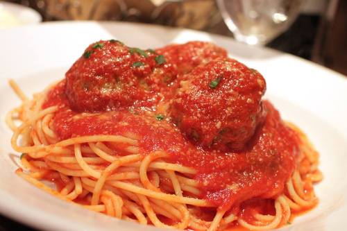 A plate of spaghetti topped with marinara sauce and two large meatballs, garnished with herbs.