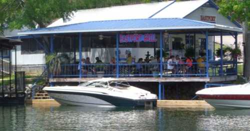 A waterfront restaurant with a blue roof, featuring outdoor seating and boats docked nearby.