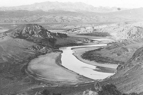 A black and white landscape featuring a winding river surrounded by mountains and rugged terrain.