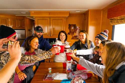 A group of friends cheerfully toasting with red cups inside a cozy camper. Smiles and laughter fill the scene.