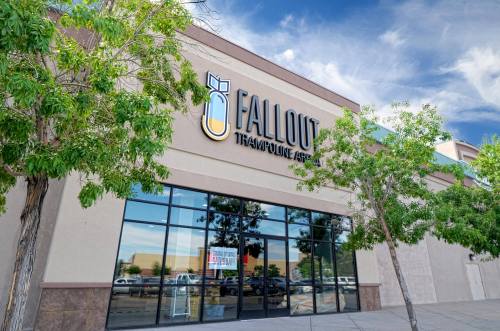 Exterior of Fallout Trampoline Park, featuring large windows and a logo, surrounded by trees and a clear blue sky.