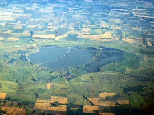 Aerial view of a large lake surrounded by patchwork farmland and fields in various shades of green and brown.