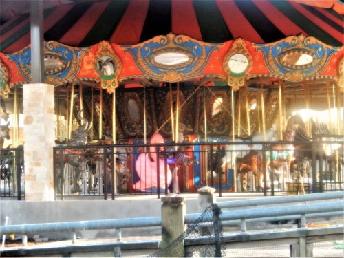 A colorful carousel with ornate decorations and horses, partially obscured by a fence.