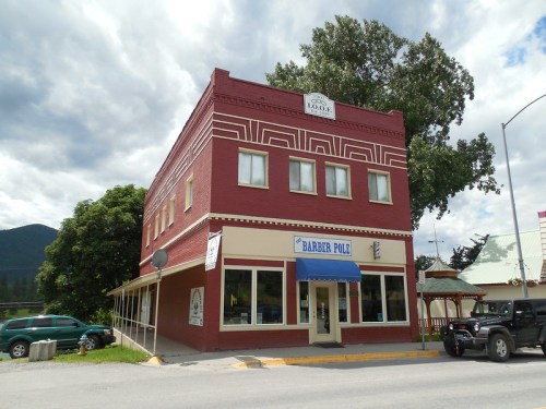 A red brick building with three stories, featuring a barber pole sign and large windows, set against a cloudy sky.