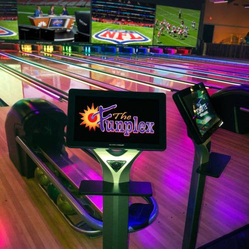 A vibrant bowling alley with colorful screens displaying sports, featuring modern bowling lanes and digital scoring systems.
