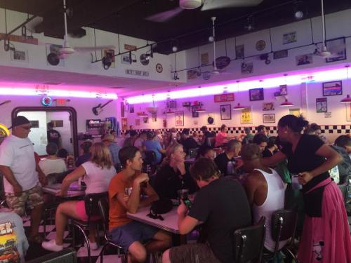 A busy diner filled with people, featuring retro decor and neon lights, creating a lively atmosphere.