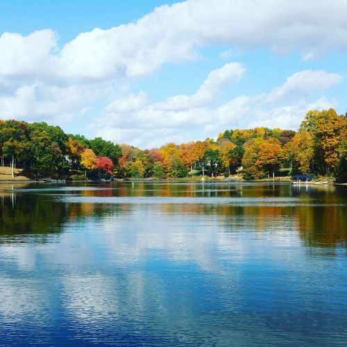 A serene lake surrounded by trees in vibrant autumn colors under a partly cloudy sky.