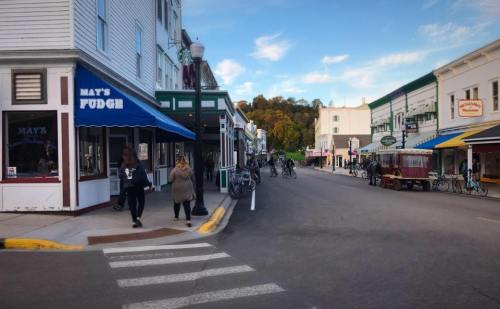 A charming street scene with shops, pedestrians, and bicycles, set against a backdrop of trees and a clear sky.