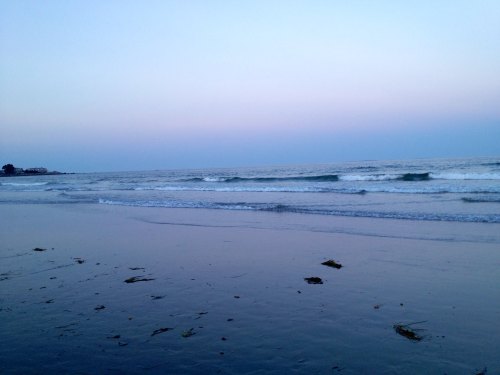A serene beach at dusk, with gentle waves lapping at the shore under a pastel sky.