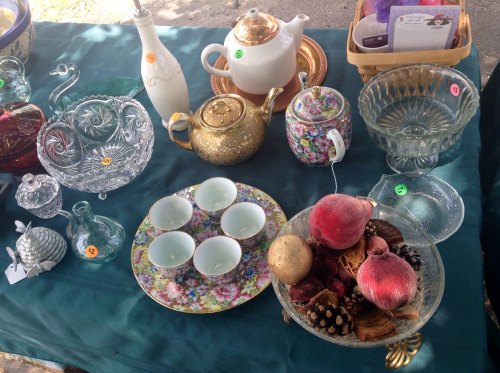 A table displaying various vintage glassware, teapots, decorative bowls, and small dishes on a green tablecloth.