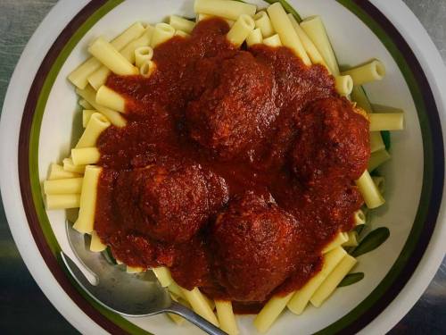 A bowl of pasta topped with meatballs and marinara sauce, served with a spoon on the side.