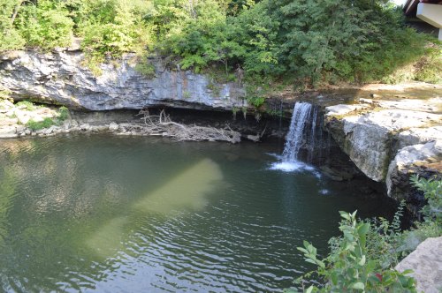 A serene waterfall cascading into a calm pool, surrounded by lush greenery and rocky cliffs.