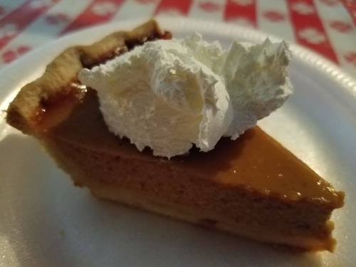 A slice of pumpkin pie topped with a dollop of whipped cream on a paper plate.