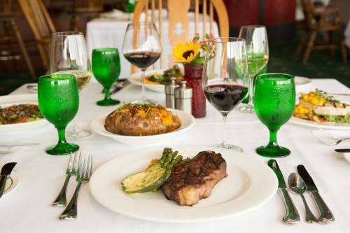A beautifully set dining table with a steak, baked potato, and salads, surrounded by green glasses and wine.