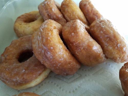 A close-up of glazed donuts stacked on a plate, showcasing their golden-brown color and shiny glaze.