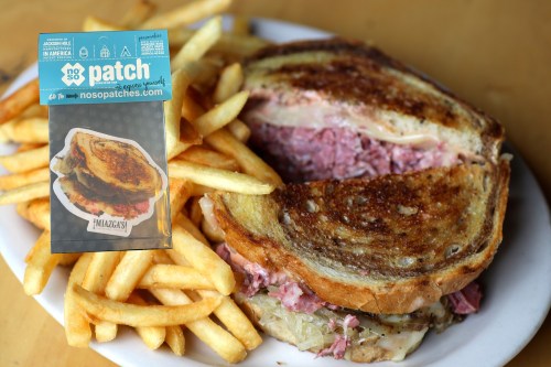 A plate of crispy fries next to a grilled sandwich filled with meat and cheese, with a promotional card in the background.