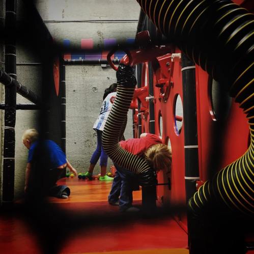 Children playing in a colorful indoor play area with tubes and climbing structures.