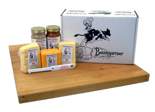 A wooden board displays a box of Baumgartner products, including jars and various cheese blocks.
