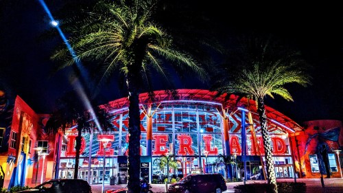 Brightly lit entrance of Deerland at night, surrounded by palm trees and colorful lights.