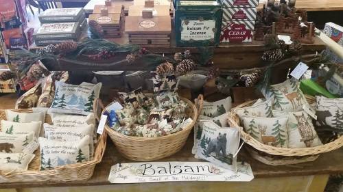 Display of decorative pillows and baskets featuring balsam products, surrounded by pinecones and festive decor.