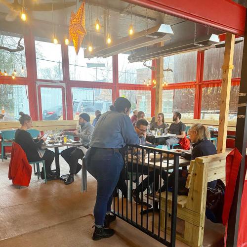 A cozy restaurant interior with patrons dining, large windows, and warm lighting creating a welcoming atmosphere.