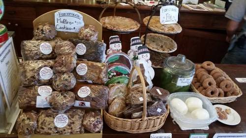 A display of assorted baked goods, including muffins, cookies, pies, and donuts, arranged on a wooden counter.