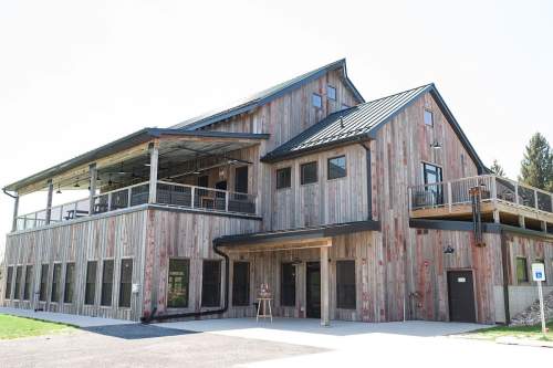 A large wooden building with multiple levels, featuring a balcony and large windows, set against a clear sky.