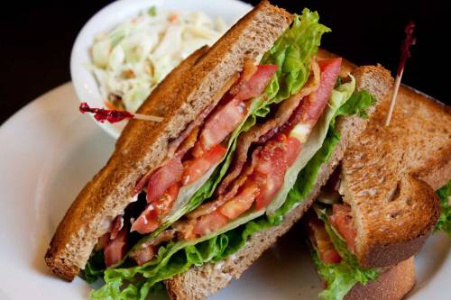 A close-up of a sandwich with bacon, lettuce, and tomato on whole grain bread, served with a side of coleslaw.