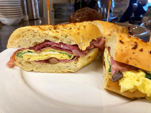 A close-up of a sandwich with layers of ham, egg, and greens on a toasted, herb-infused roll, cut in half.