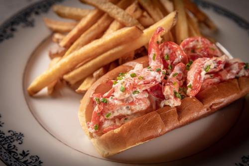 A lobster roll filled with lobster salad, served with a side of golden French fries on a decorative plate.