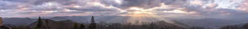 A panoramic view of mountains under a dramatic sky with rays of sunlight breaking through the clouds.