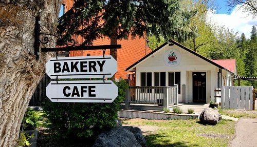 A quaint bakery and cafe with a signpost, surrounded by trees and a sunny blue sky.