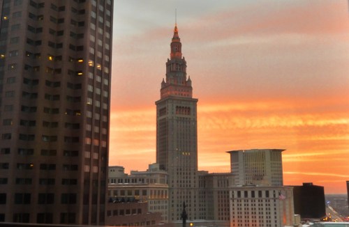 A city skyline at sunset, featuring a tall, historic tower illuminated against a colorful sky.