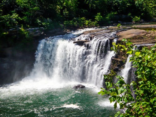 A beautiful waterfall cascading into a serene pool, surrounded by lush greenery and rocky terrain.